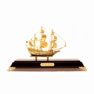 A golden wealth ship model displayed on a sleek dark wooden base with gold accents. The ship features intricately designed sails, masts, and decorative elements symbolizing prosperity and success. This Feng Shui item is crafted in gold to represent wealth and is often used to attract good fortune and abundance. The base includes an engraved plaque, adding a touch of elegance to this powerful symbol of financial growth.