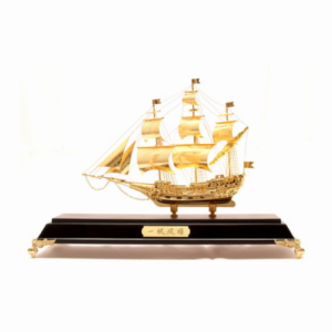 A golden wealth ship model elegantly displayed on a dark wooden base with gold decorative accents. The ship features detailed sails, masts, and rigging, crafted to symbolize prosperity and successful ventures. This Feng Shui wealth ship is designed to attract abundance, financial growth, and good fortune, making it a powerful decorative item. The base includes a gold plaque, enhancing its luxurious appearance and auspicious symbolism.