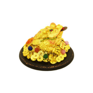 A golden three-legged Feng Shui money frog sits atop a pile of coins and jewels on a decorative round base. The frog holds a coin in its mouth, symbolizing wealth and prosperity. The body of the frog is adorned with intricate details and colorful gems, representing abundance and good fortune.